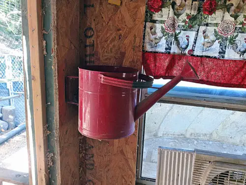 Red watering can mounted as decorative chicken coop storage