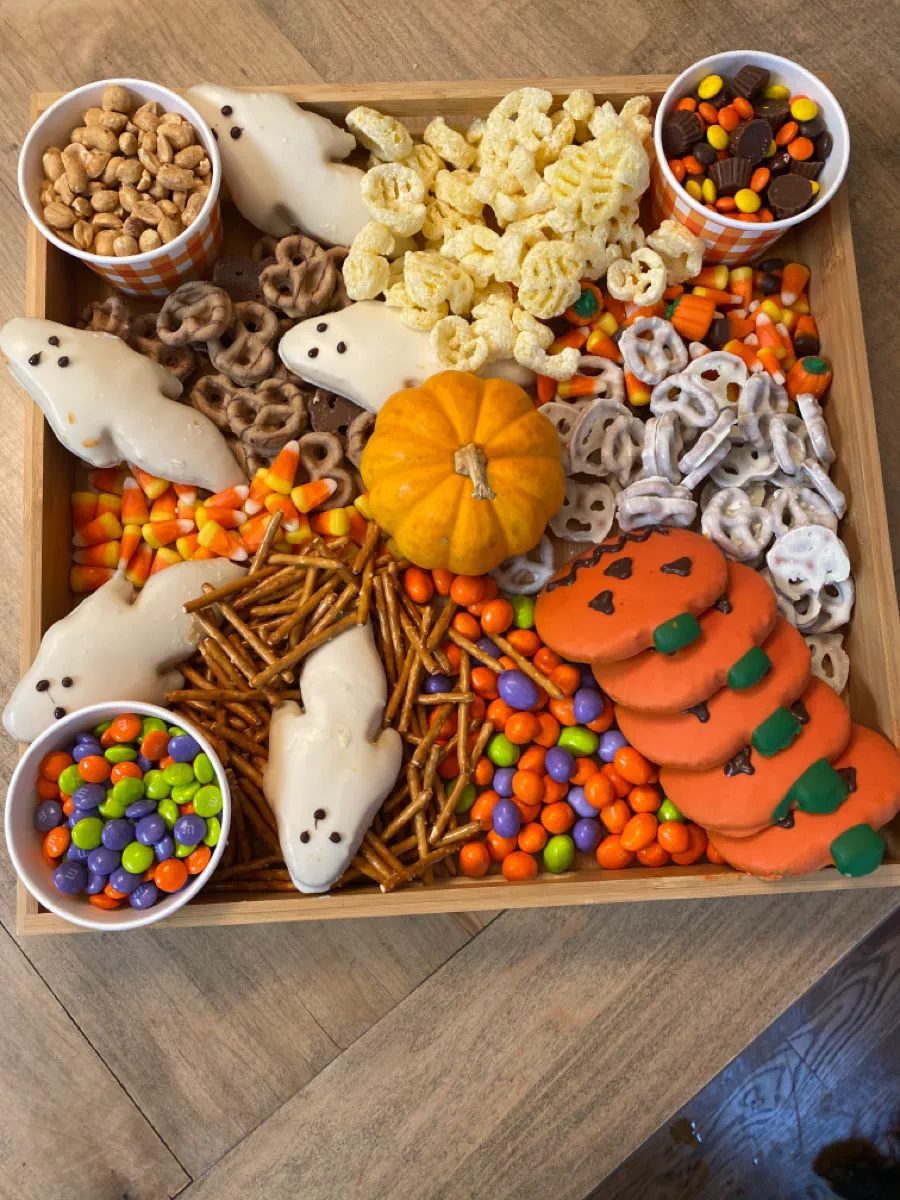 41 Spooky Dessert Board Ideas for Halloween Parties 8 Halloween snack board with ghost cookies, pumpkin cookies, pretzels, candy corn, and colorful chocolates