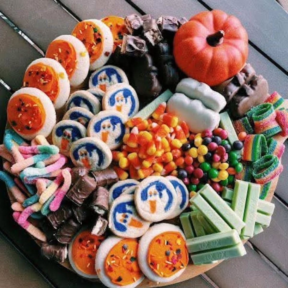 41 Spooky Dessert Board Ideas for Halloween Parties 12 Colorful Halloween candy board with frosted cookies, gummy worms, candy corn, chocolate, and mint sticks