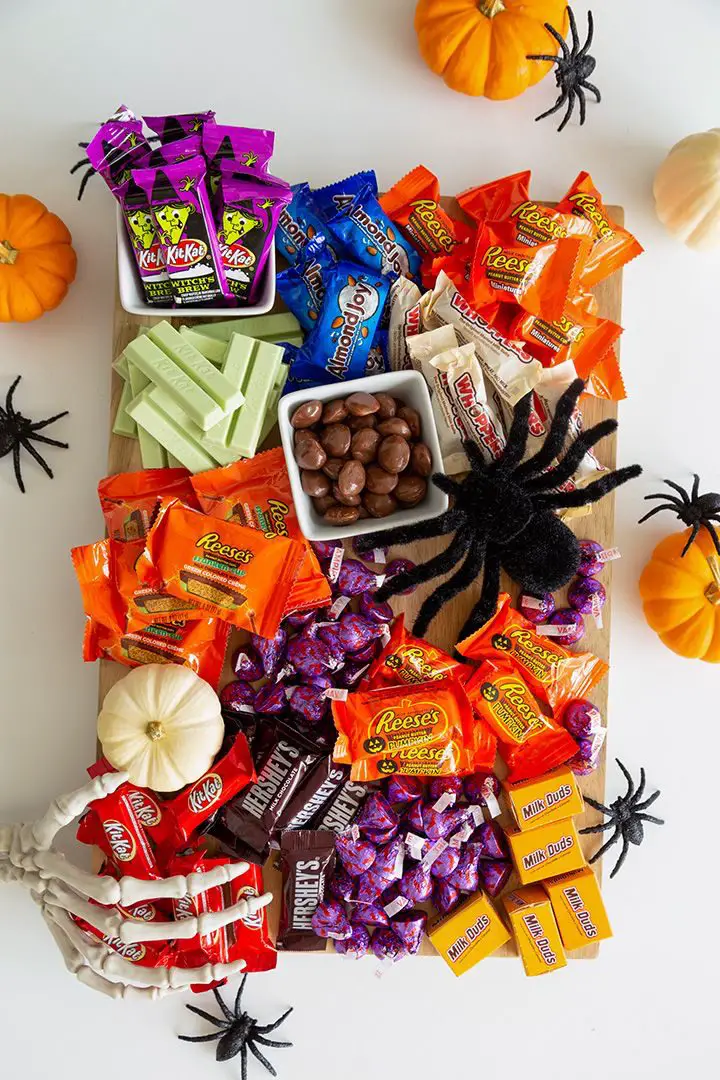 41 Spooky Dessert Board Ideas for Halloween Parties 15 Halloween chocolate candy board with wrapped chocolate bars, mint chocolates, peanut butter cups, and spider decorations