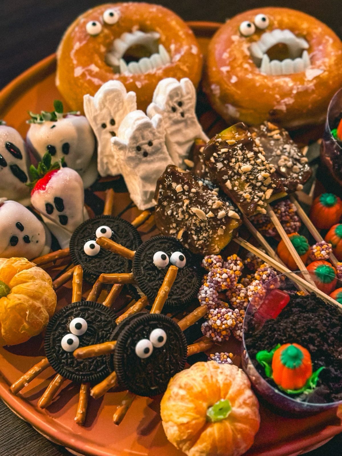 41 Spooky Dessert Board Ideas for Halloween Parties 16 Monster Halloween dessert board with donuts, ghost strawberries, marshmallows, Oreo spiders, and caramel apple treats